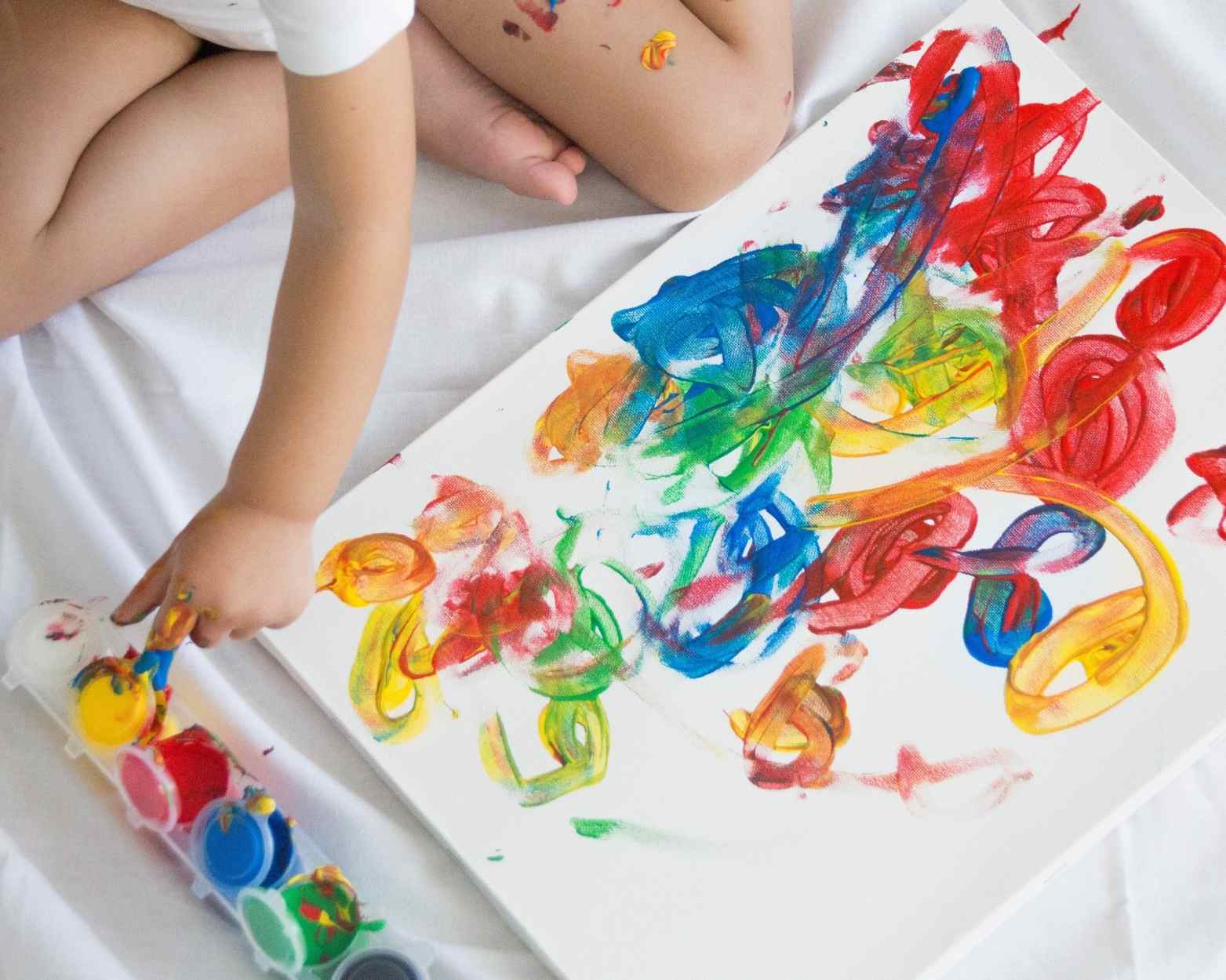 A toddler using finger paint to paint a canvas on a sheet which is a mom hack.