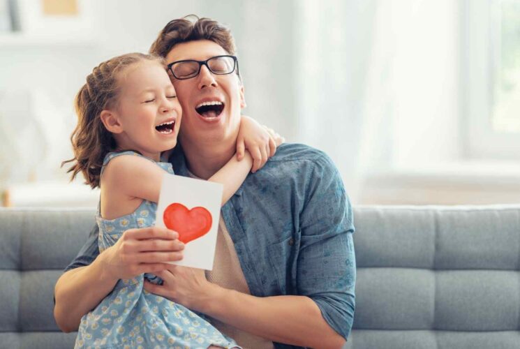 A daughter hugging her dad on father's day after giving him his fathers day gift and card.