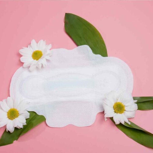 An all natural cotton organic pad for periods next to some daisies.