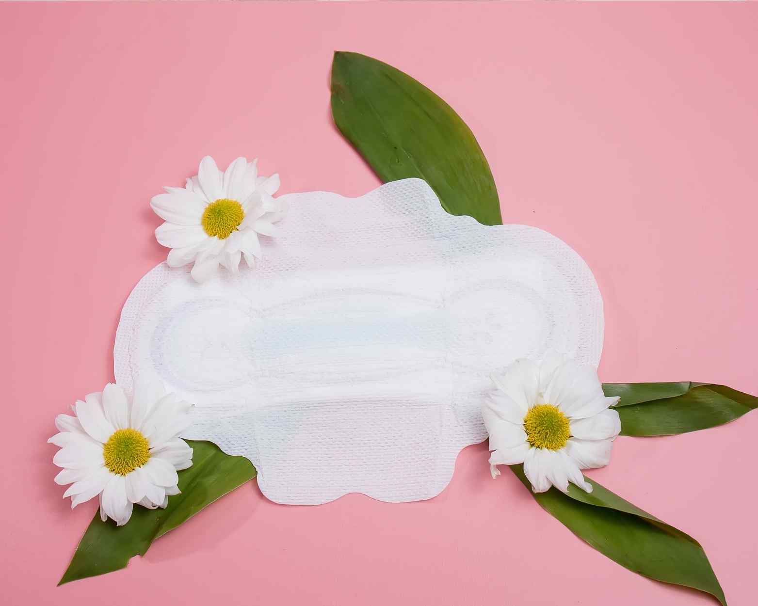 An all natural cotton organic pad for periods next to some daisies.