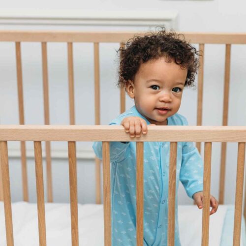 A baby boy in his bamboo pajamas standing in his crib.
