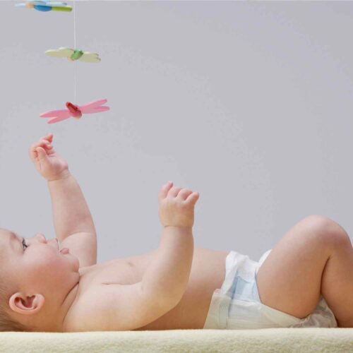A newborn baby reaching up to play with his developmental newborn toys.