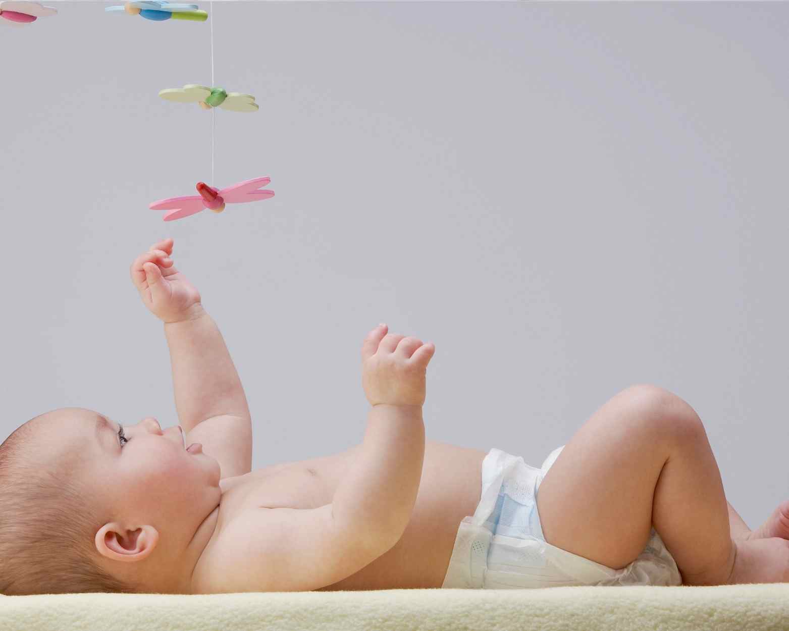 A newborn baby reaching up to play with his developmental newborn toys.