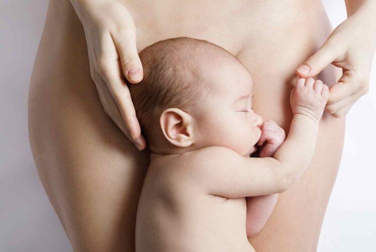 A postpartum mom showing her postpartum body with her newborn baby.