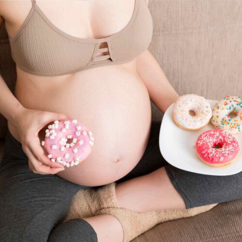 A pregnant woman holding donuts but wanting to have healthy pregnancy snacks instead.