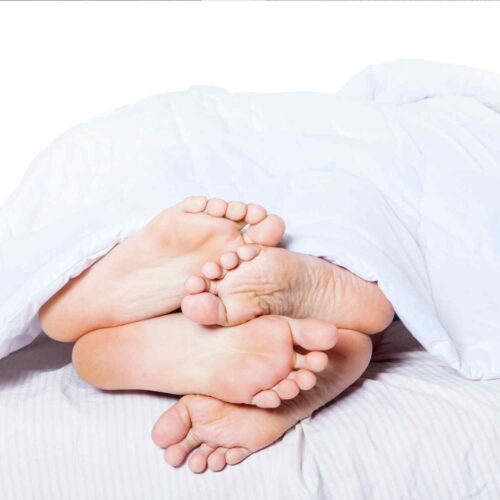 A pair of feet under a bed sheet.