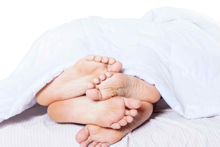 A pair of feet under a bed sheet.