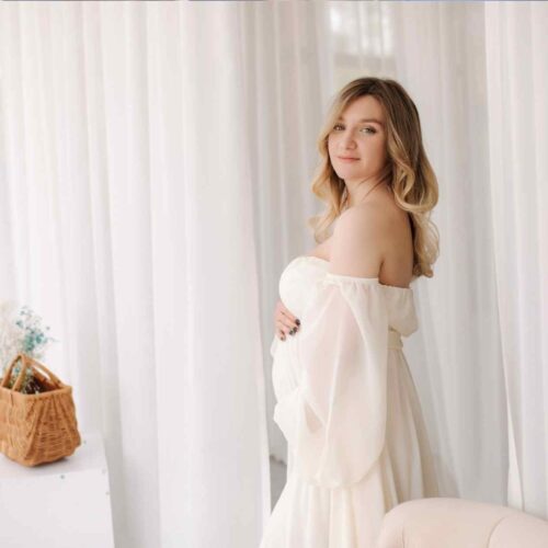 A woman having her maternity photoshoot with a gorgeous white flowy maternity dress.
