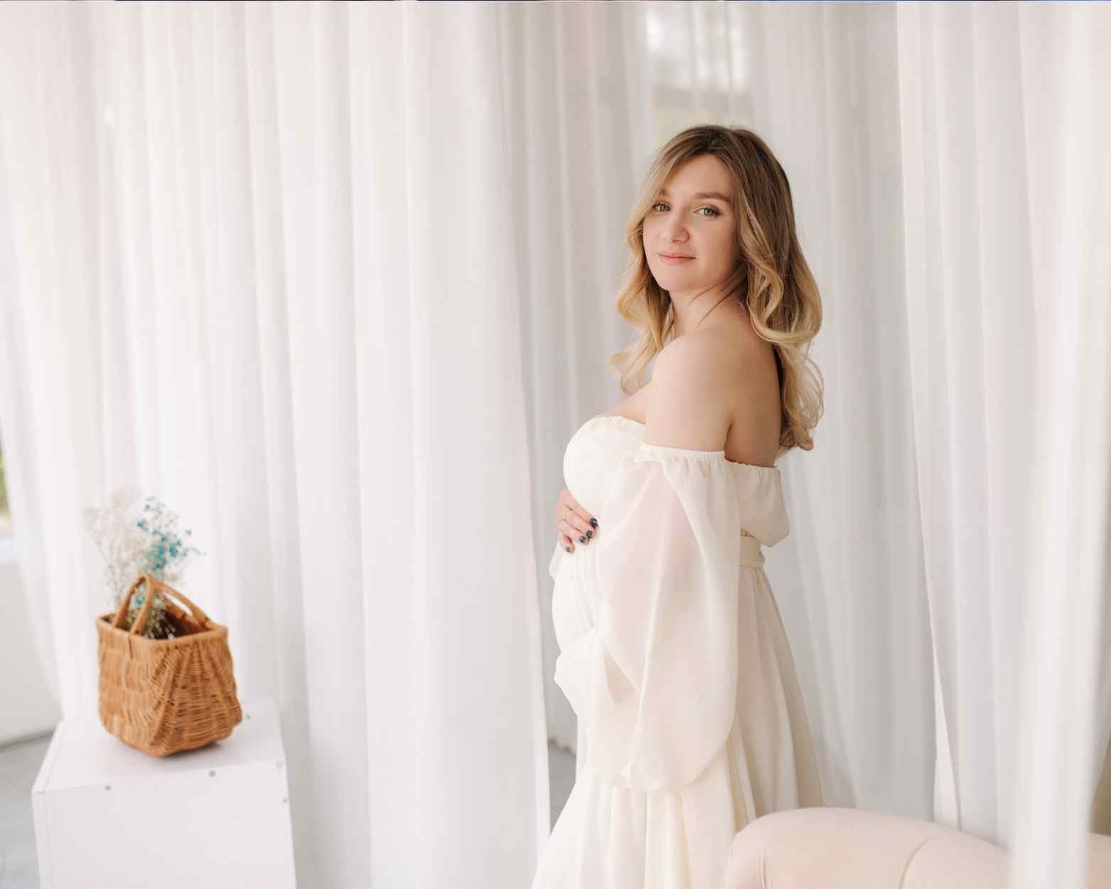 A woman having her maternity photoshoot with a gorgeous white flowy maternity dress.
