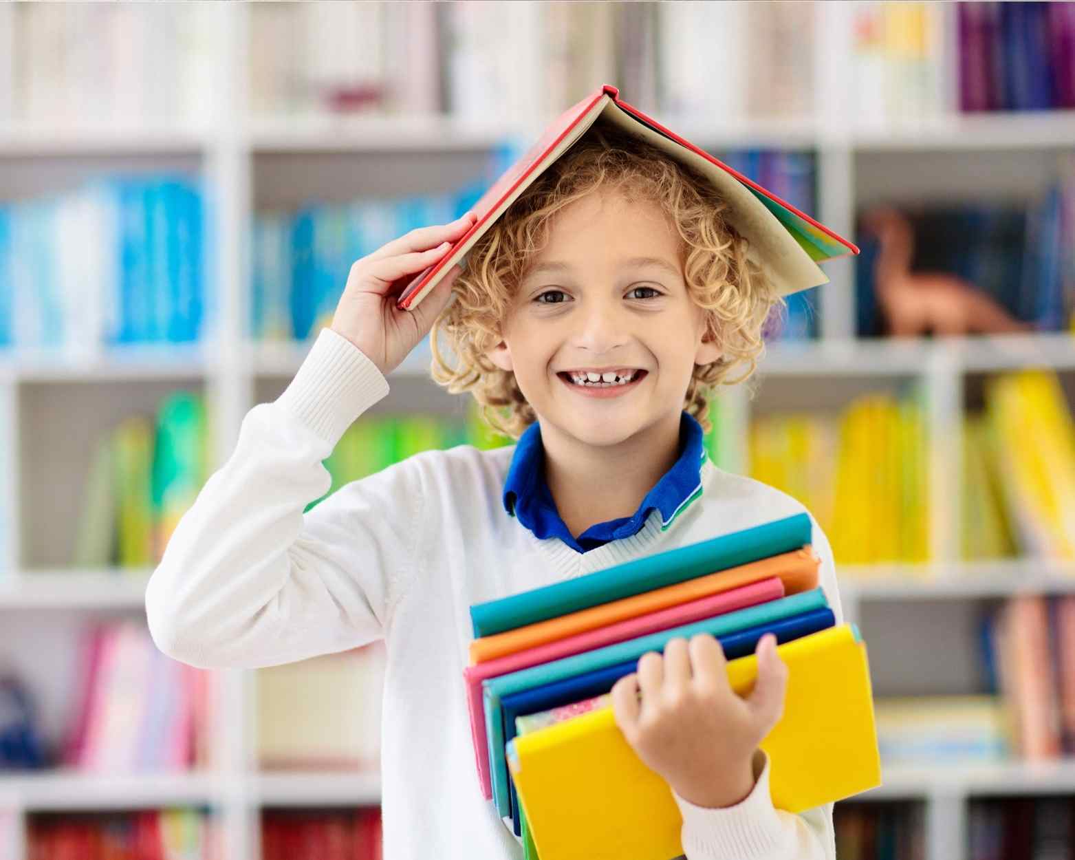 A toddler boy with a book on his head and in his hands because an adult is teaching him how to read with a phonics program.
